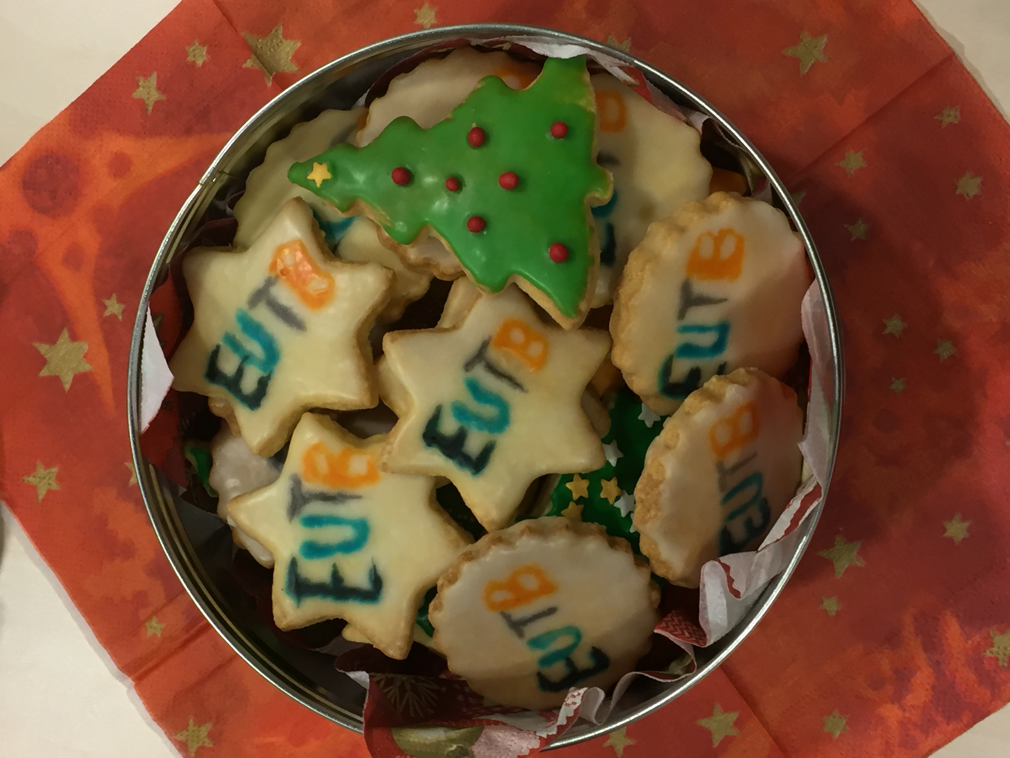 Runde Dose mit sternförmigen Keksen, die das EUTB-Logo zeigen. Ebenfalls gibt es tannenbaumförmige Kekse. Die Keksdose steht auf einer roten Serviette mit Sternen.
