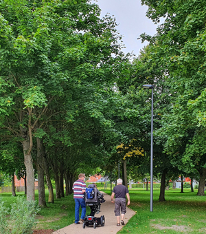 Drei Personen bei einem Spaziergang durch den Park, eine von ihnen sitzt in einem elektrischen Rollstuhl.