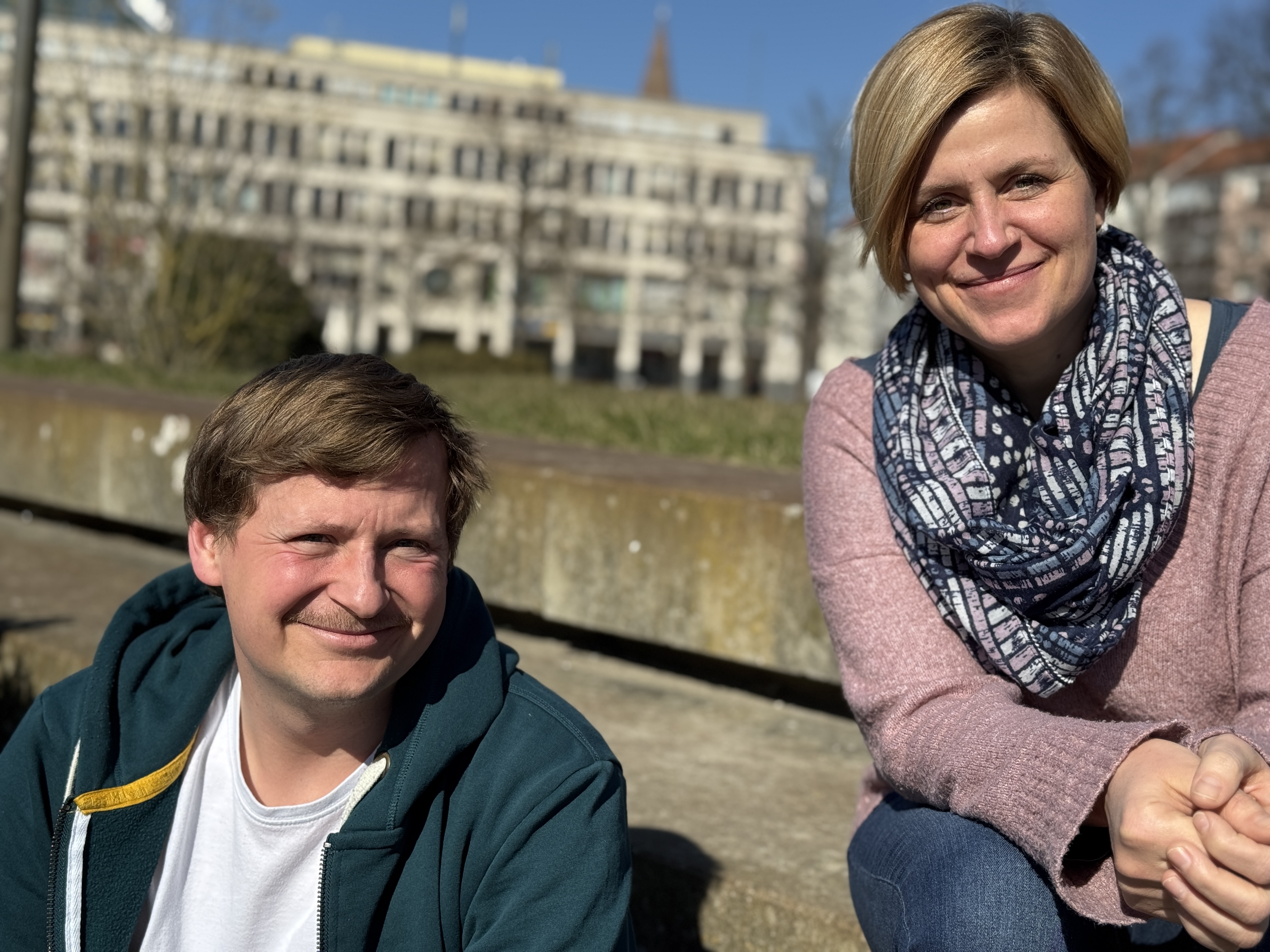 Ein Mann und eine Frau sitzen und schauen freundlich in die Kamera